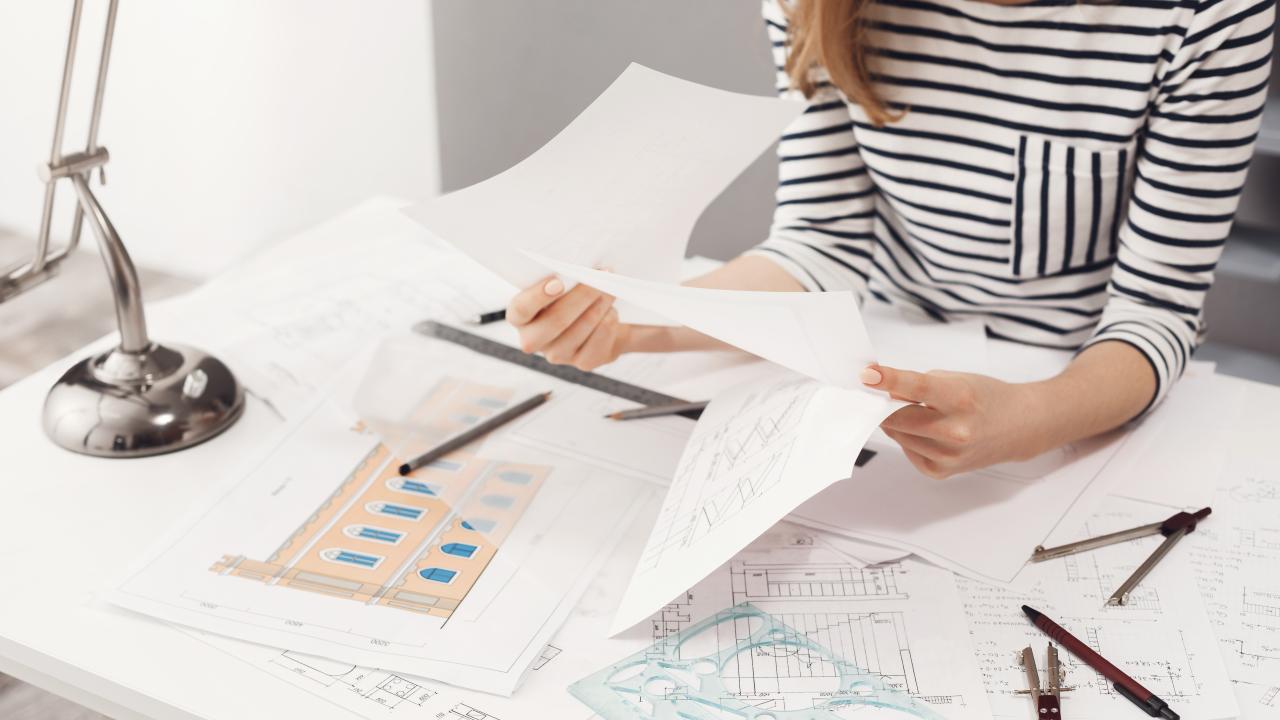 close-up-detail-female-engineer-wearing-striped-clothes-sitting-white-big-table-looking-through-papers-working-construction-project